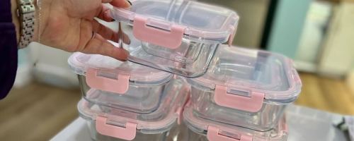 hand holding clear and pink glass food storage containers on kitchen counter