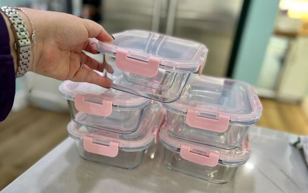hand holding clear and pink glass food storage containers on kitchen counter