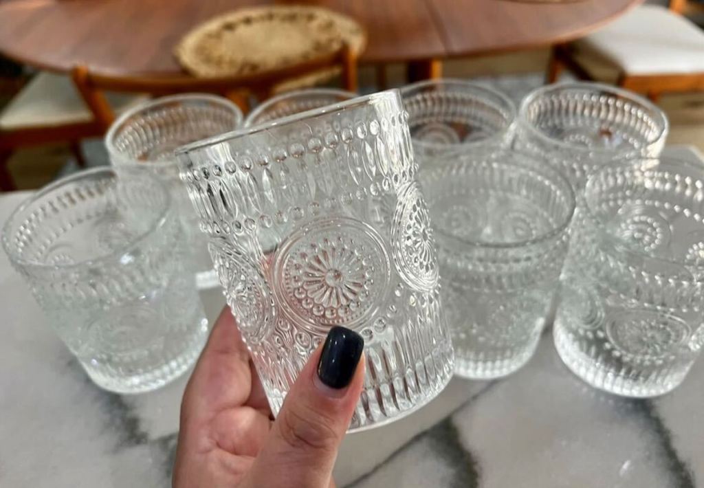 hand holding clear glass with matching vintage drinkware on counter