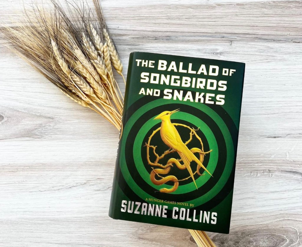 the ballard of songbirds and snakes book sitting on wood surface with tall wheat grass stems