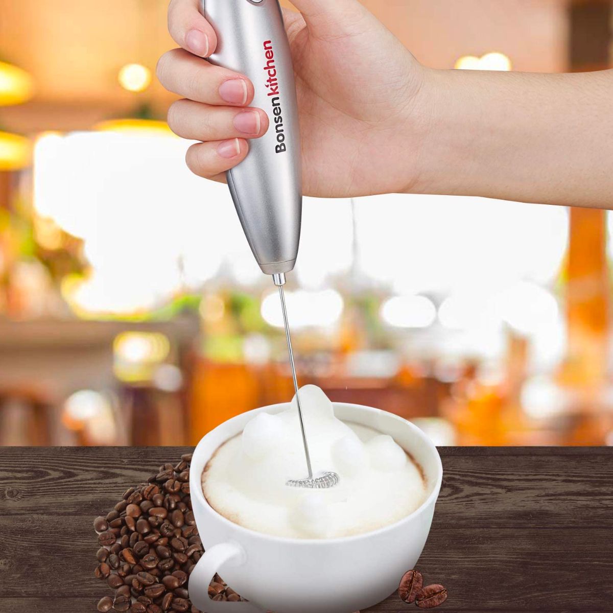 a woman's hand holding a bonsen kitchen milk frother and frothing milk for a cappucino