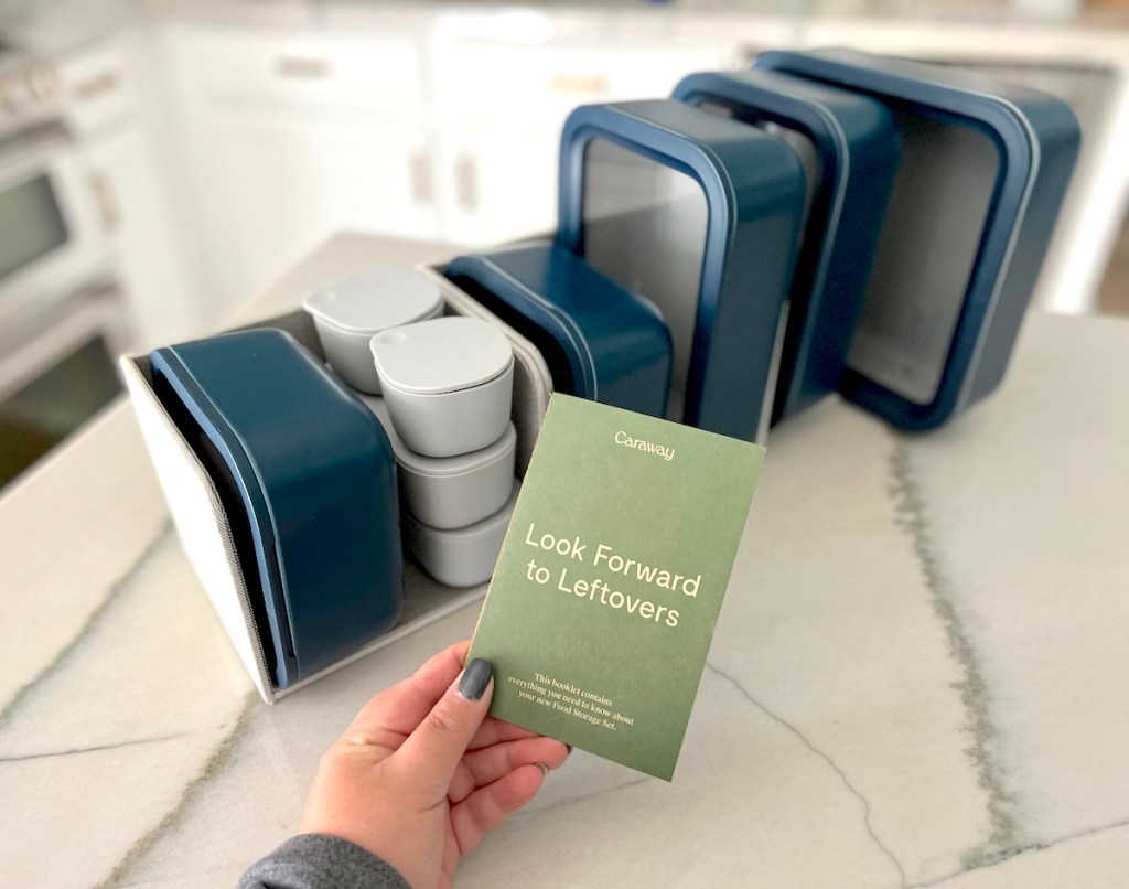 hand holding pamphlet in front of organized navy containers on white marble kitchen countertop