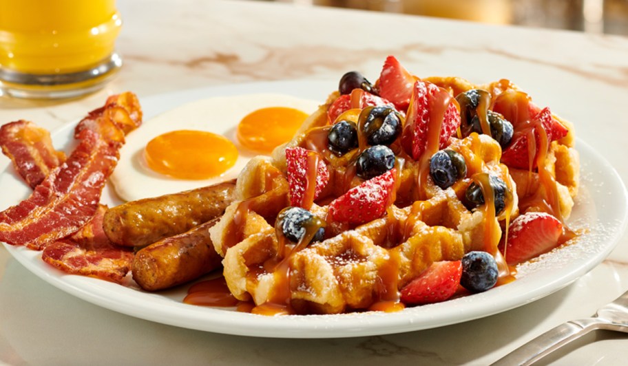 waffles topped with berries next to eggs bacon and sausage