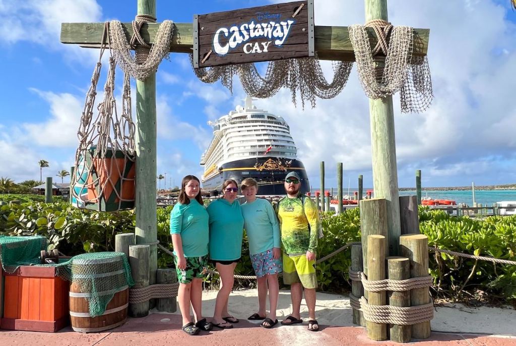family standing under disney castaway cay cruise sign with ship in ocean