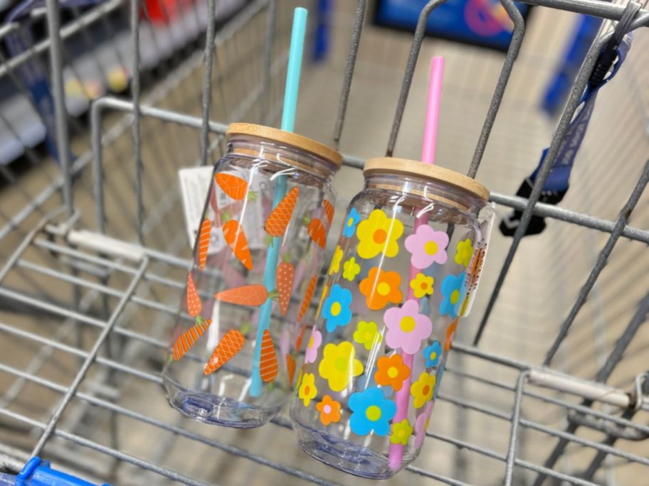 two plastic easter glasses with wooden lids and straws. One with a carrot pattern and one with a floral print