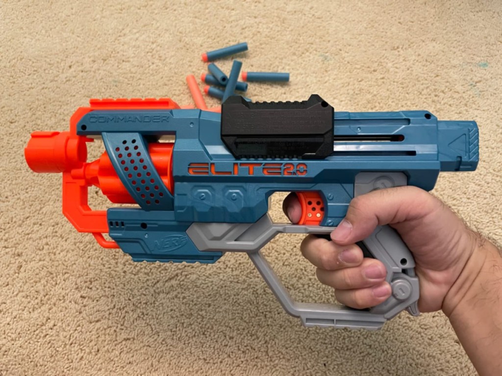 hand holding a nerf commander blaster above a tan rug