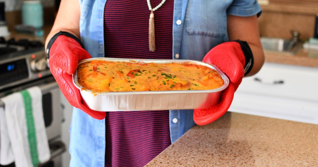 Costco pre-made enchilada bake out of the oven with red oven mitts. 