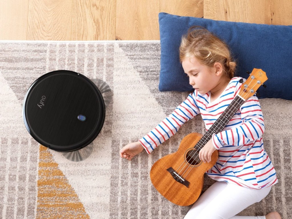 girl sleeping with small guitar next to robot vacuum