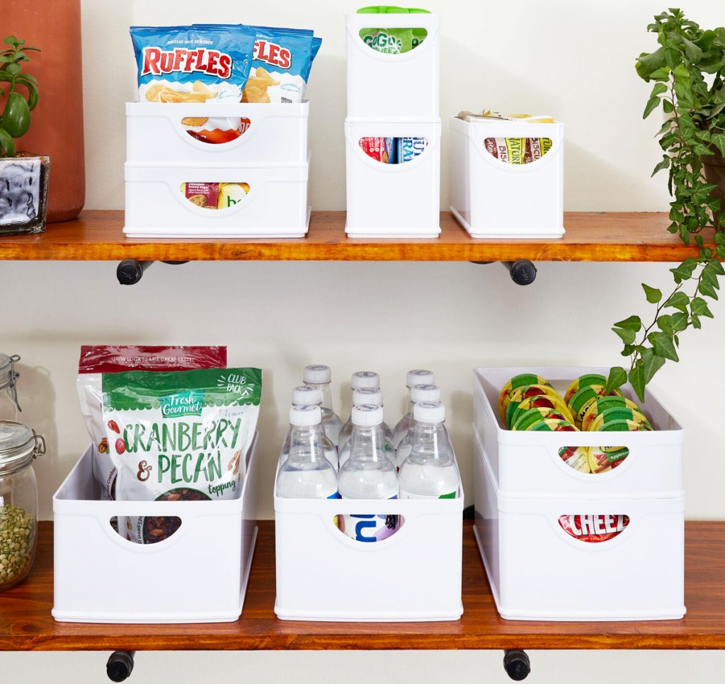 multiple white storage bins with food and drinks inside on wood shelves