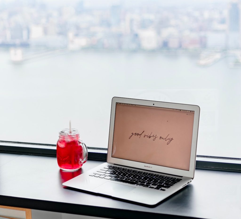 laptop with red iced drink on desk overlooking city