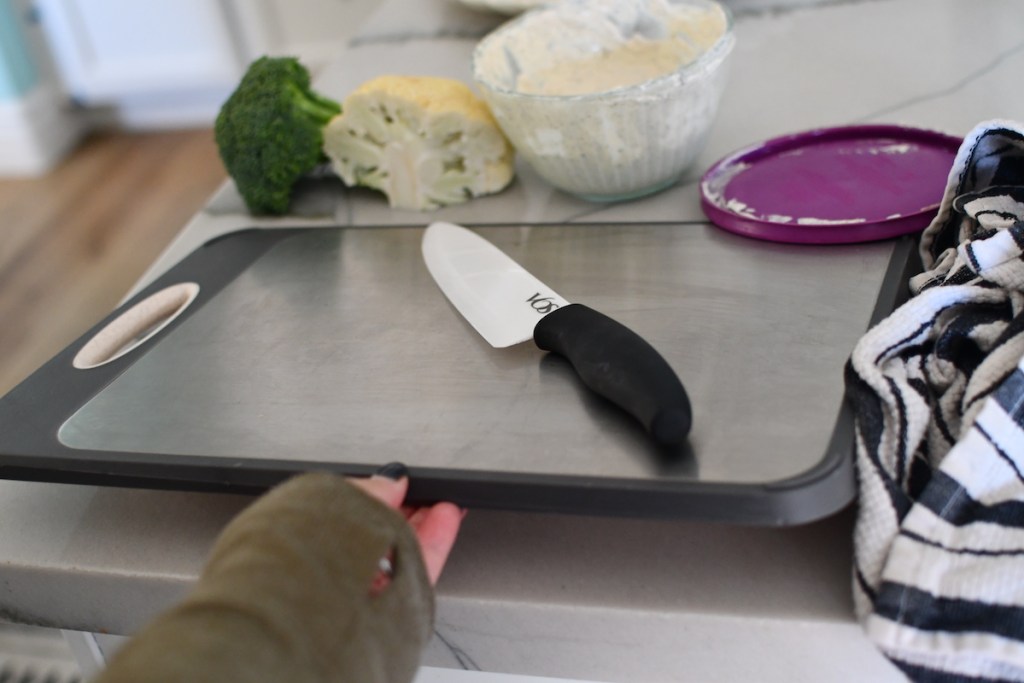 hand holding up cutting board with knife on kitchen counter