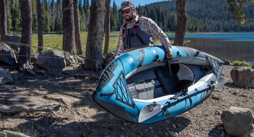 man holding Aquaglide Chinook 90 Inflatable Kayak through the woods