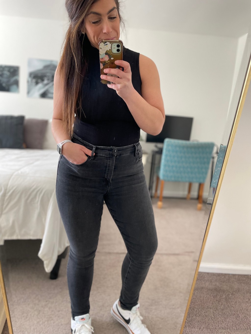 woman taking mirror selfie in nikes black bodysuit and jeans