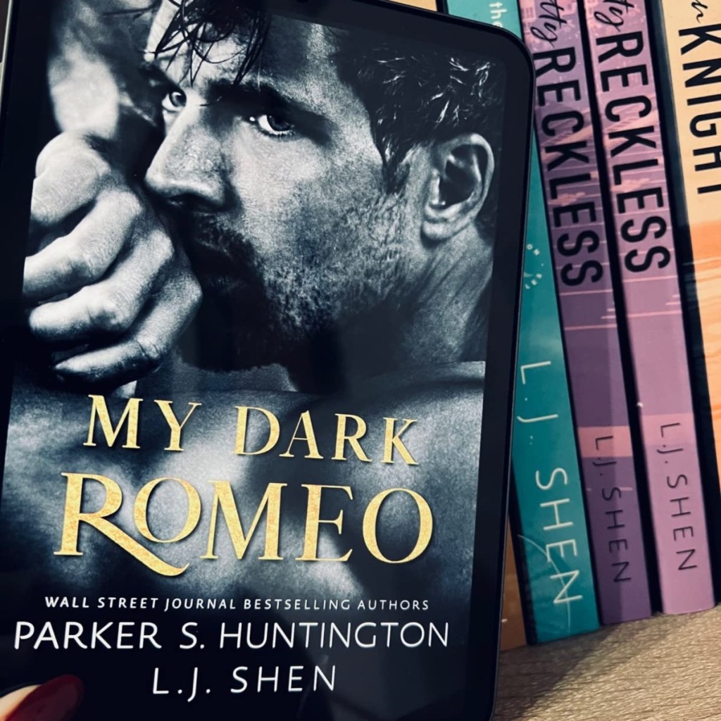holding a kindle with the cover of a My Dark Romeo on the display