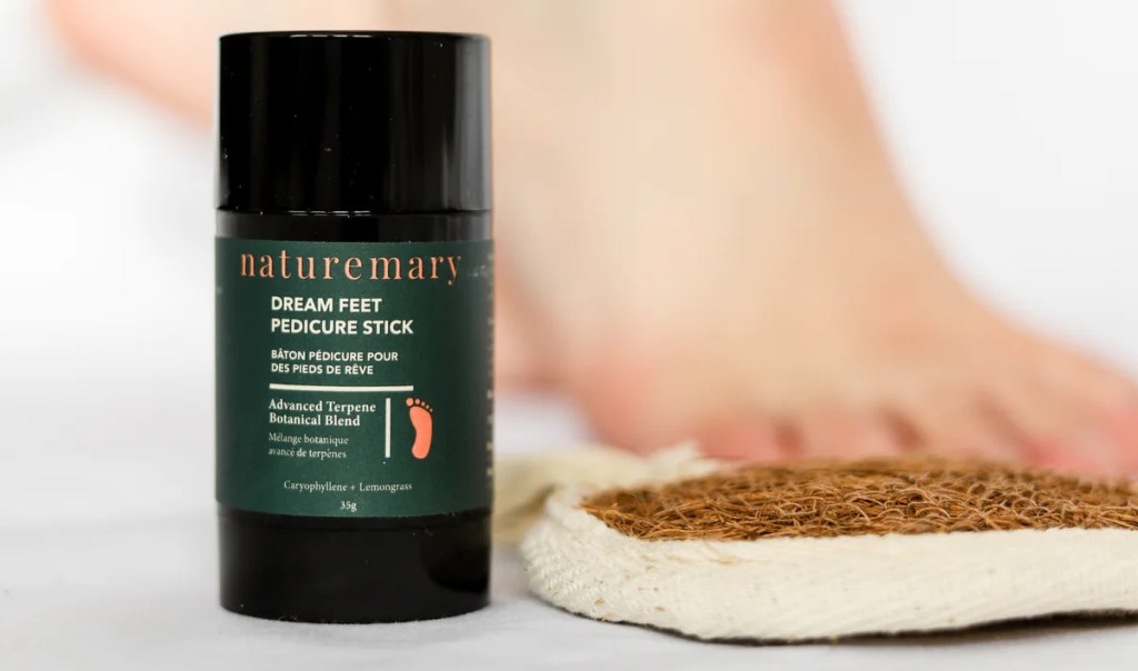 container of naturemary dream feet pedicure stick next to a loofah in front of a foot