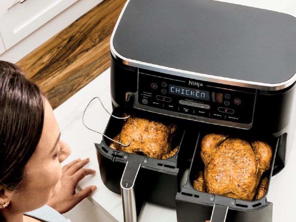 ninja double air fryer with two whole chickens inside and woman opening baskets