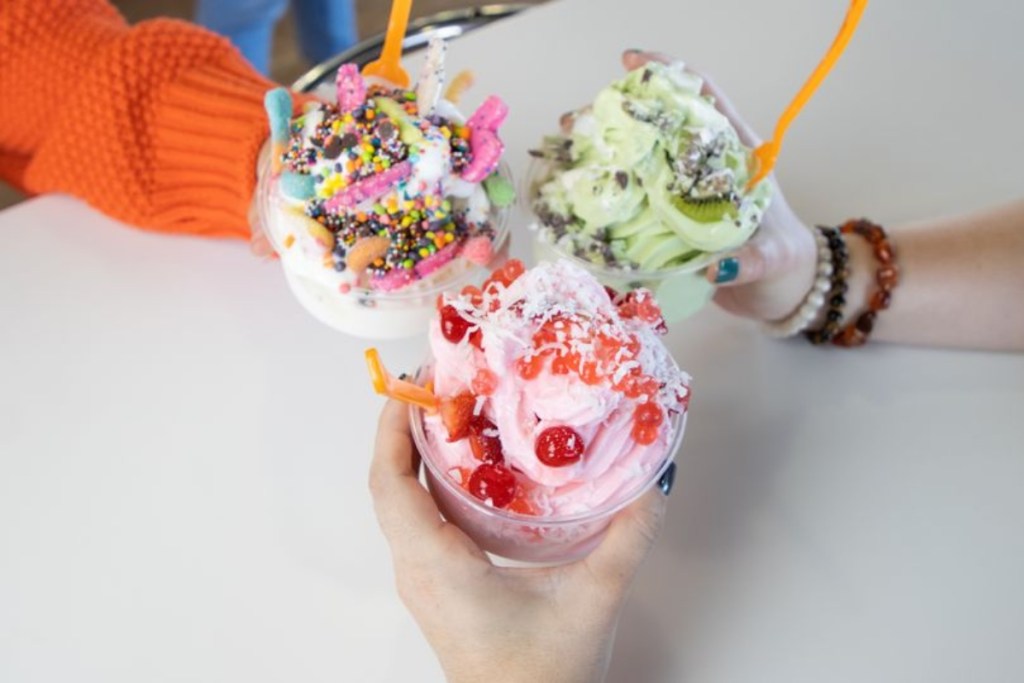three hands holding cups of frozen yogurt with orange spoons