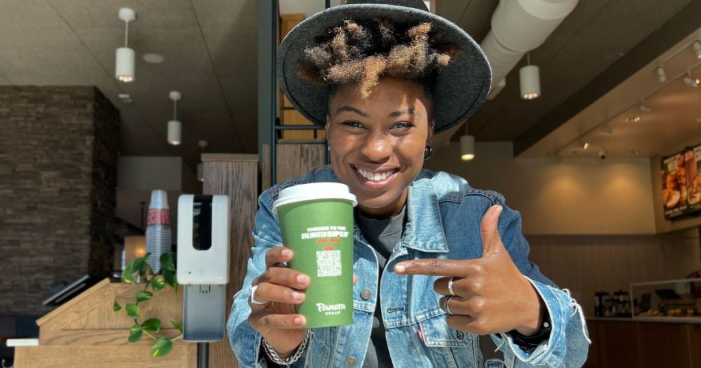 woman wearing a hat holding a panera coffee cup