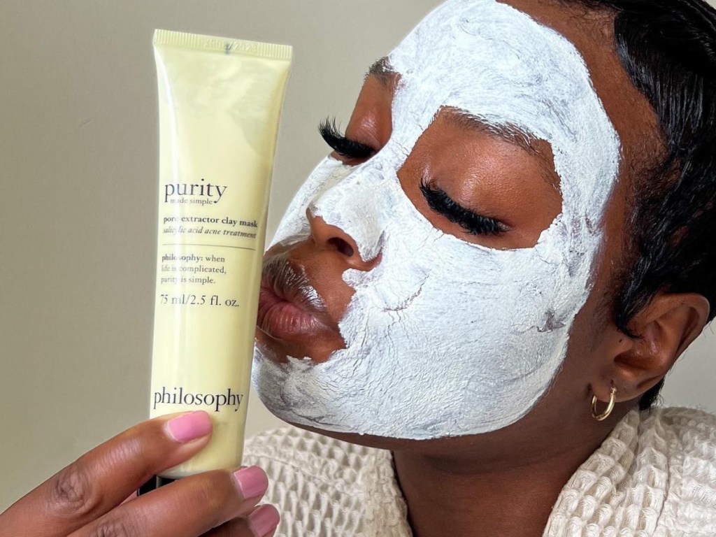 woman with clay face mask kissing skincare product