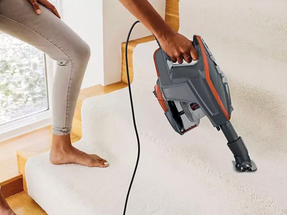 woman using hand shark vac on carpeted stairs