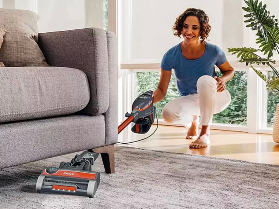 woman using orange and gray shark vacuum under couch in living room