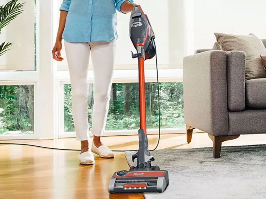 woman using gray and orange shark vacuum on carpet and hardwood floor in living room
