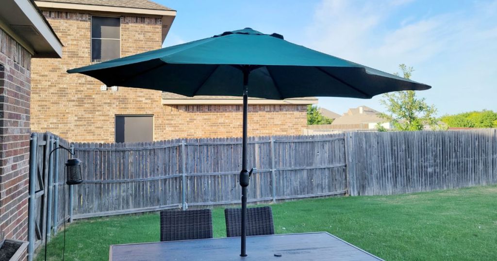 patio table with 2 chairs and green umbrella in yard with wood fence