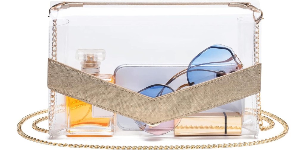 stock image of Vorspack Clear Crossbody Bag with gold accent with sunglasses. perfume and lipstick