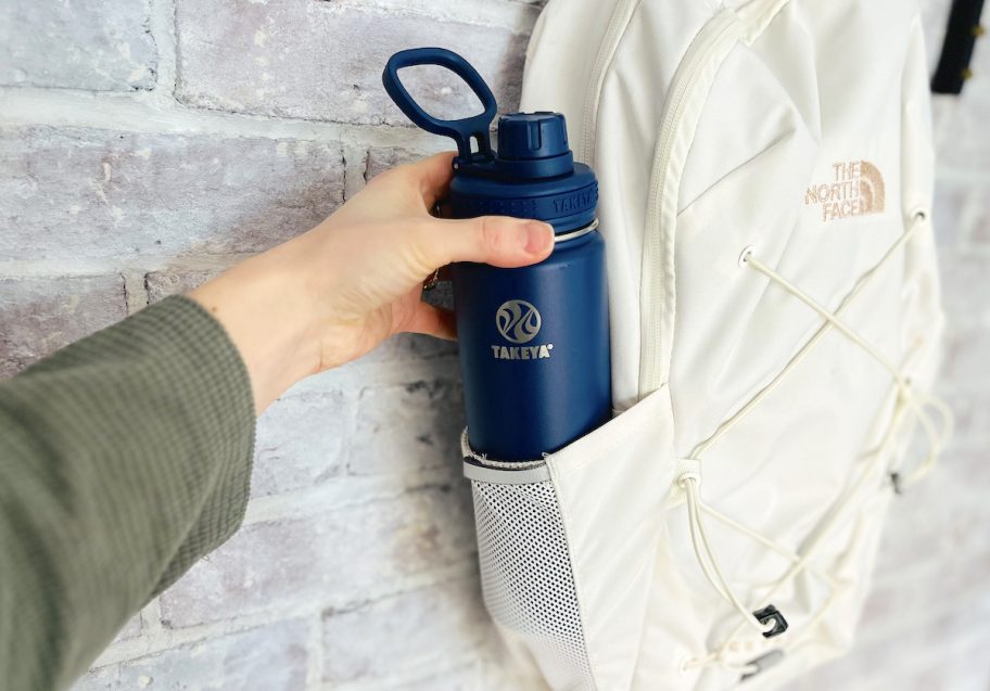 hand pulling navy blue takeya water bottle out of white the north face bookbag