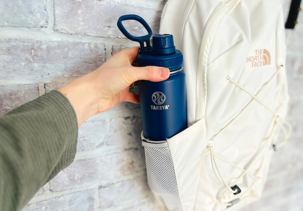 hand pulling navy blue takeya water bottle out of white the north face bookbag