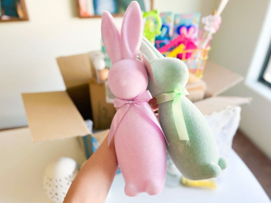 a hand displaying two flocked easter bunnies - a pink one and a mint green one