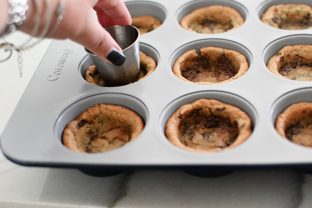 using a small cup to smash middle of cookies in a muffin tin