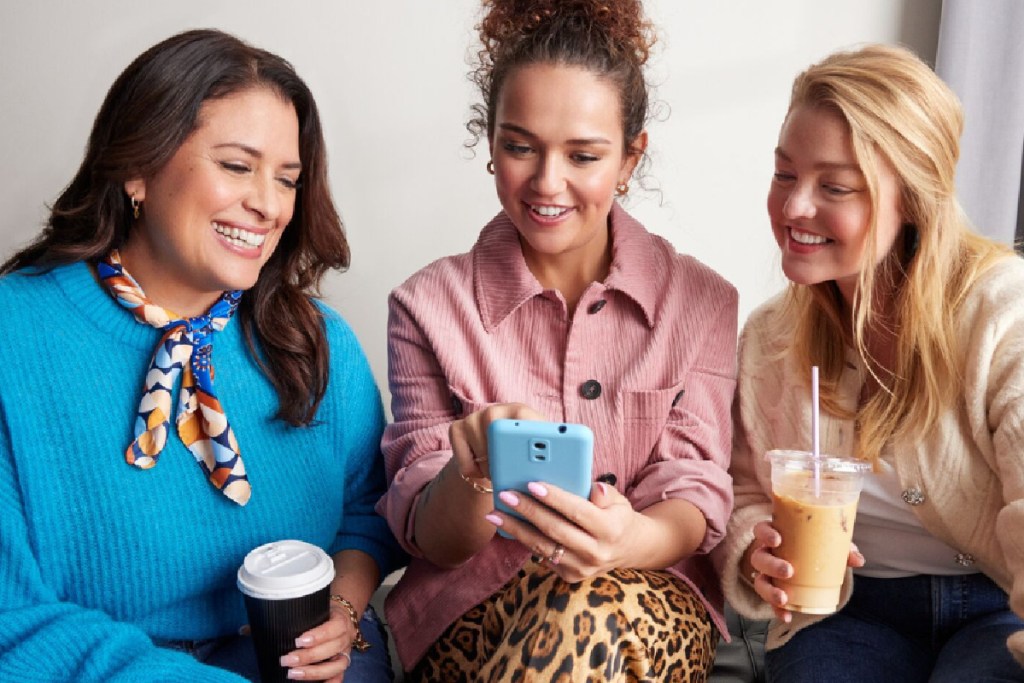 three women sitting together holding phones and coffee