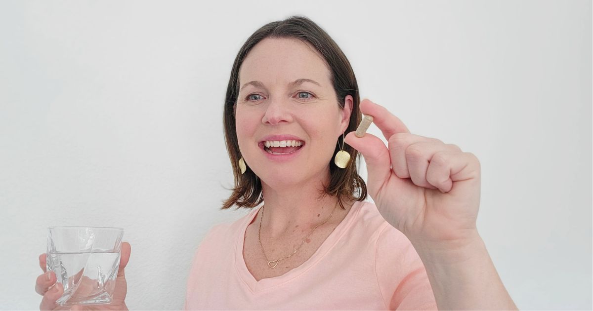 woman holding a Raw Science Perfect Skin capsule and a glass of water