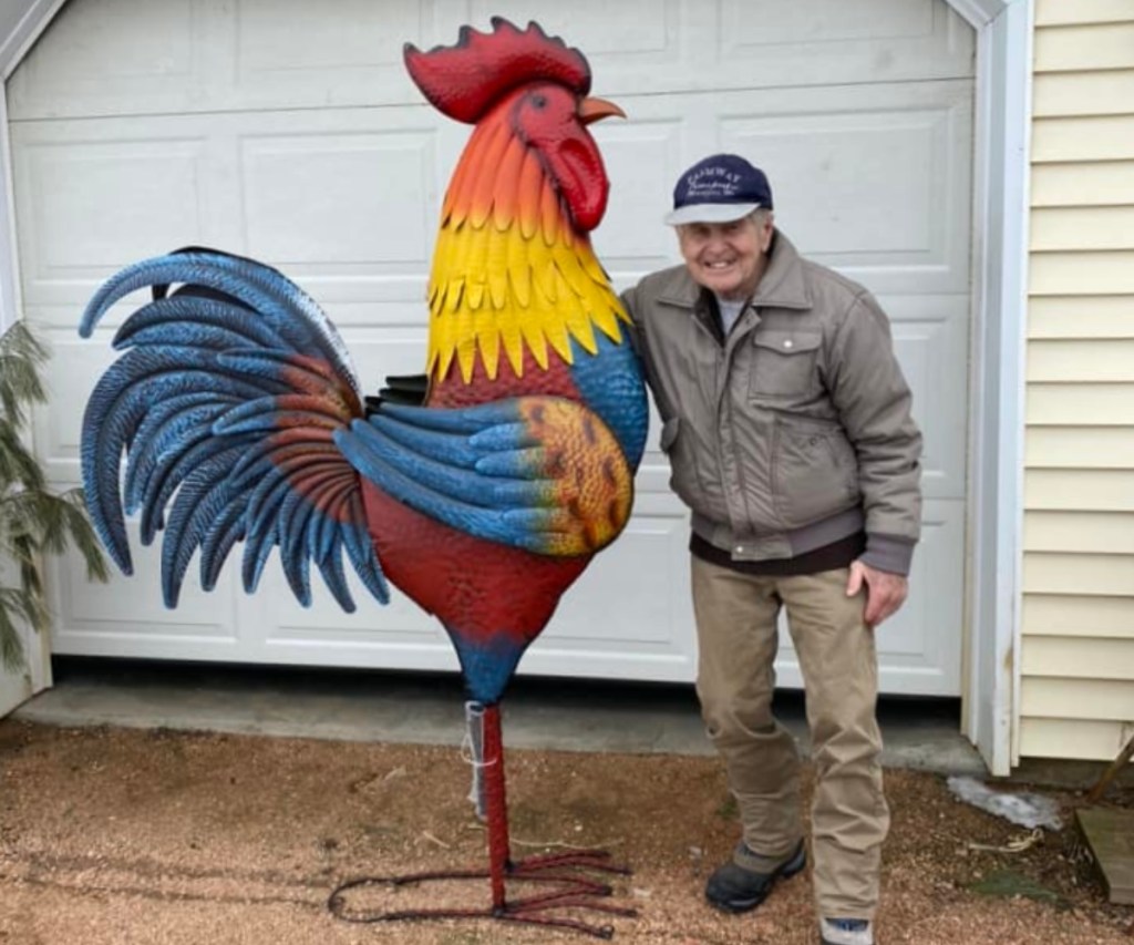 man standing with 6-foot-tall chicken statue