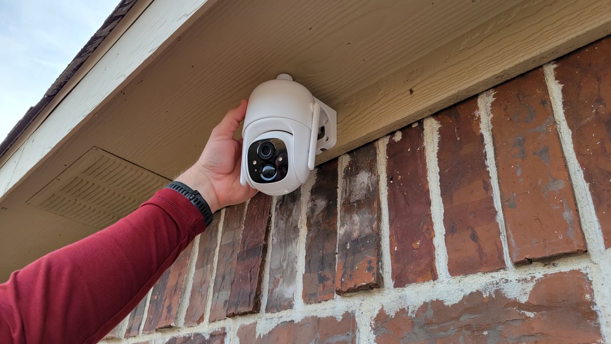 Hand holding a security camera on the side of a house