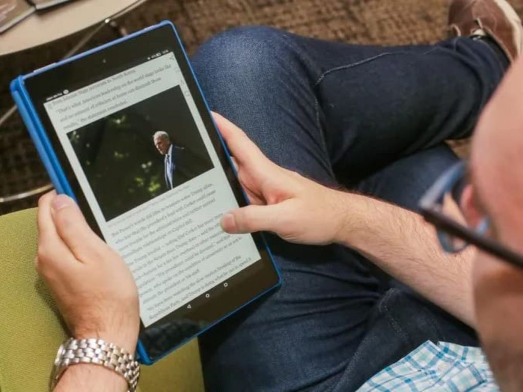 man holding an Amazon Fire HD 10 Tablet and reading a news story