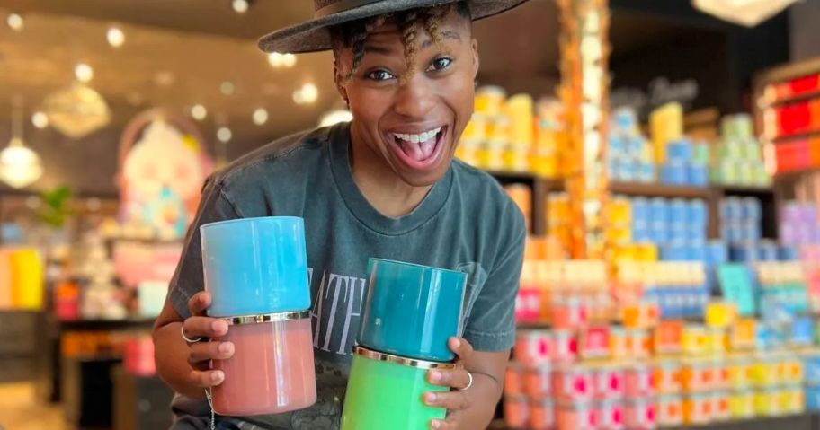 A woman with 4 BBW 3 wick candles in her hands in a bath & body works store