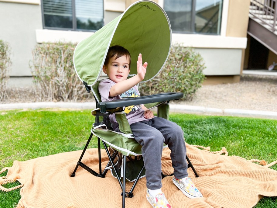 boy sitting in a green portable chair outside on a blanket