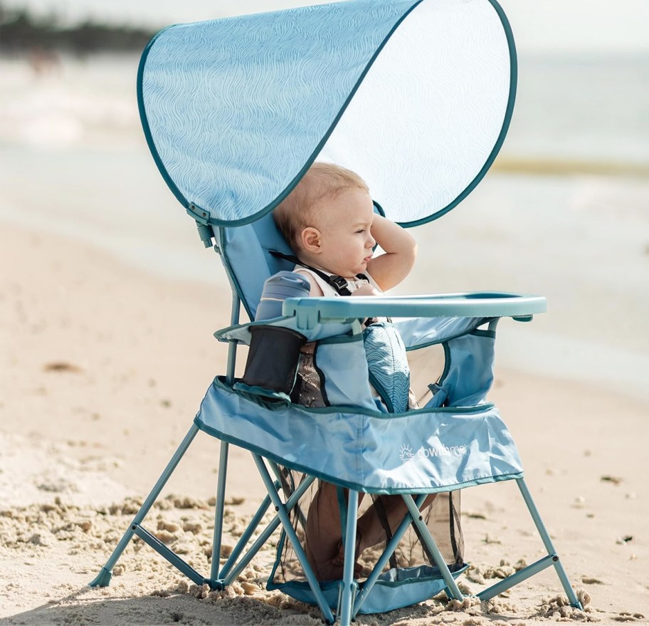 baby standing inside a portable chair on the beach