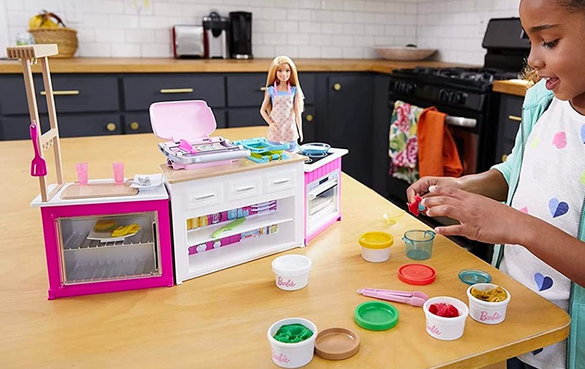 a little girl in a kitchen playing with Barbie ultimate kitchen