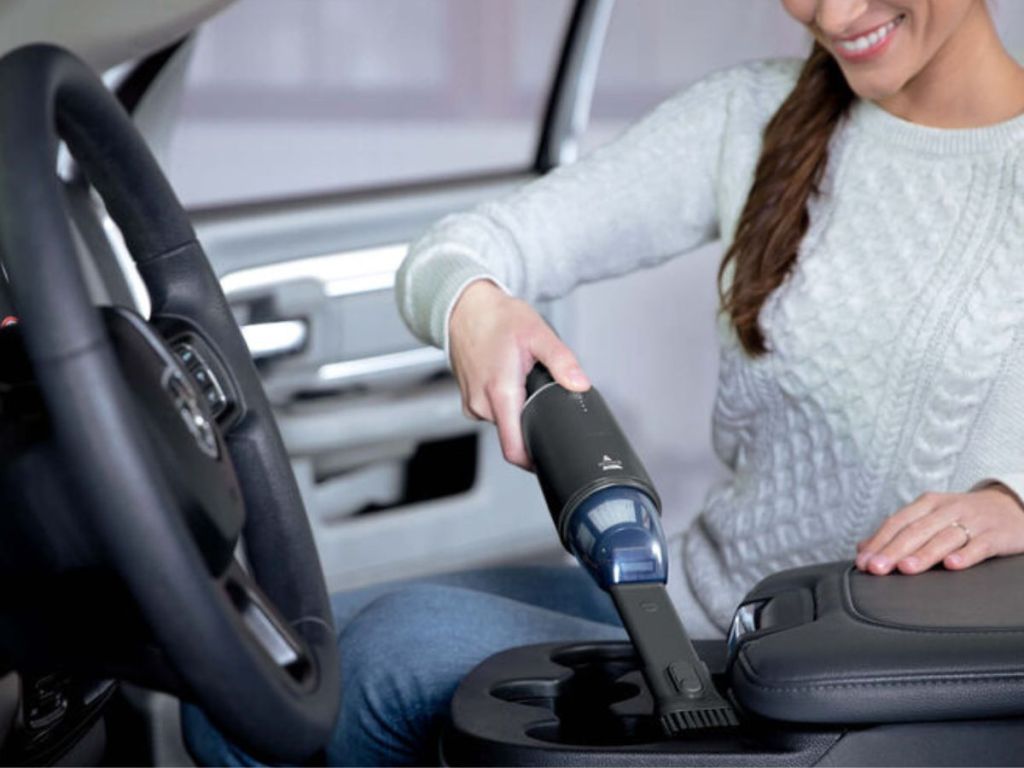 Woman cleaning inside her car with a Bissel Aeroslim Hand Vac
