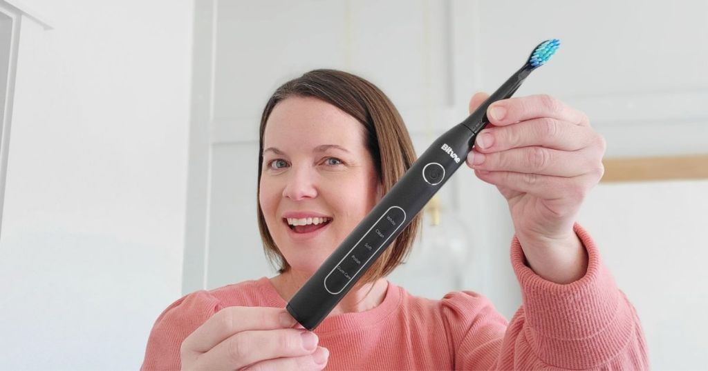 woman wearing pink top holding black electric toothbrush