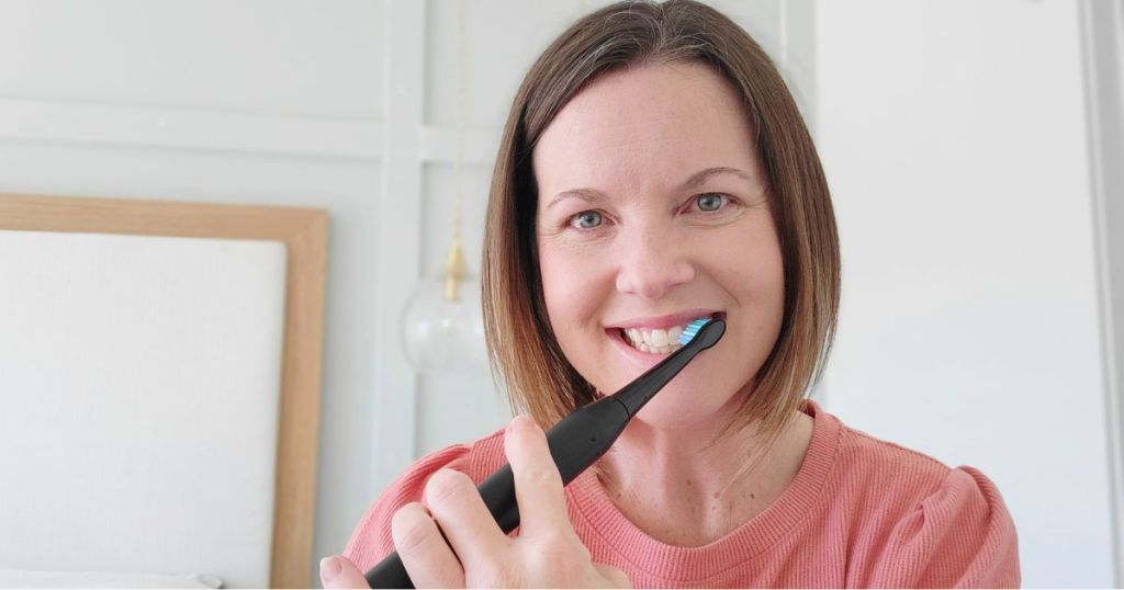 woman brushing teeth with black electric toothbrush