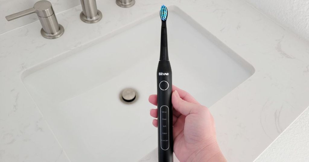 hand holding black Bitvae electric toothbrush with sink in background
