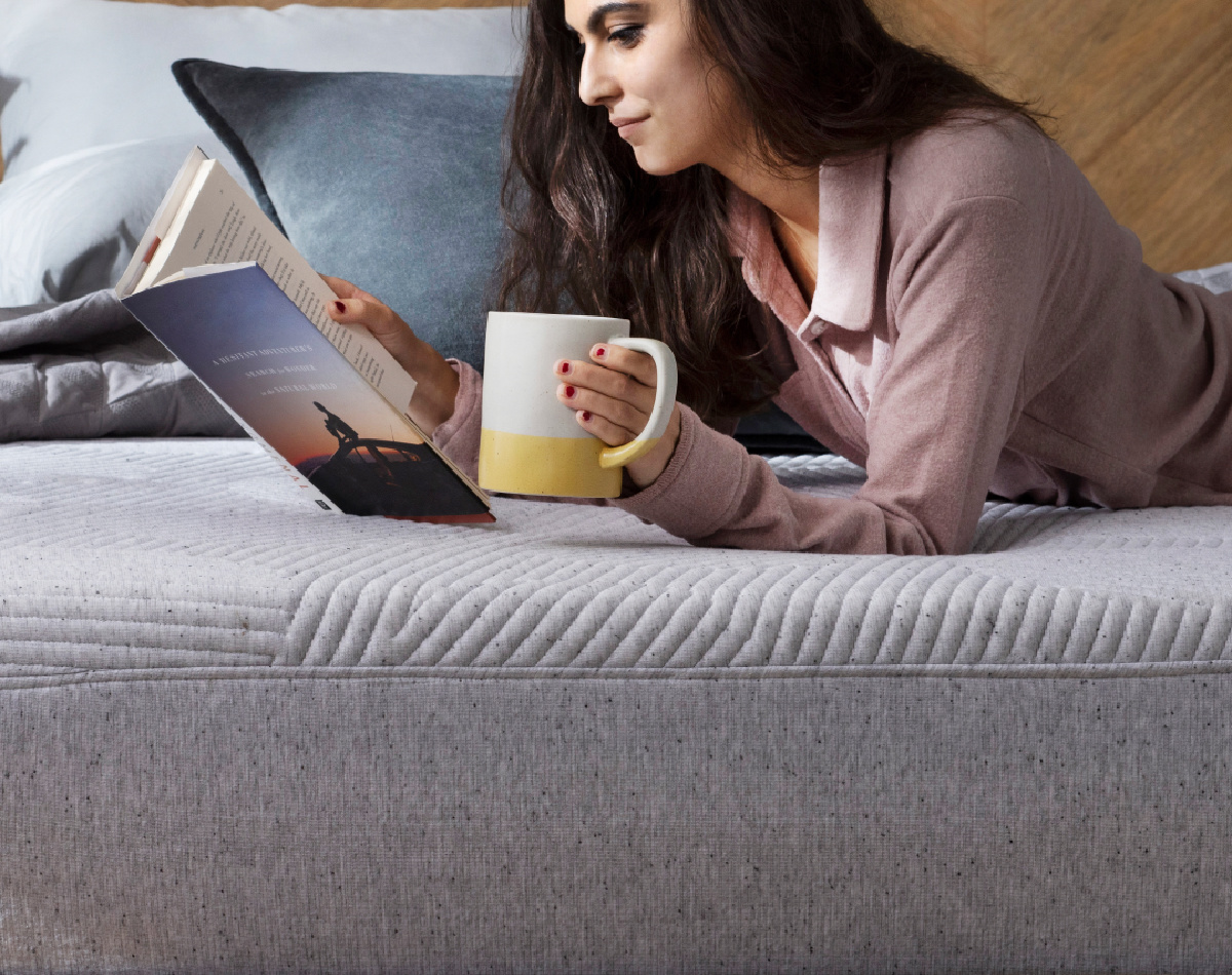 woman on mattress with laptop and coffee mug
