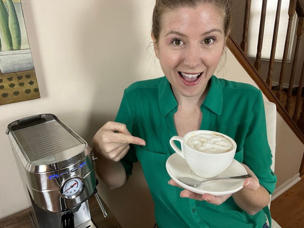 woman holding a cup with a frothy cappuccino while pointing at it and making an excited face