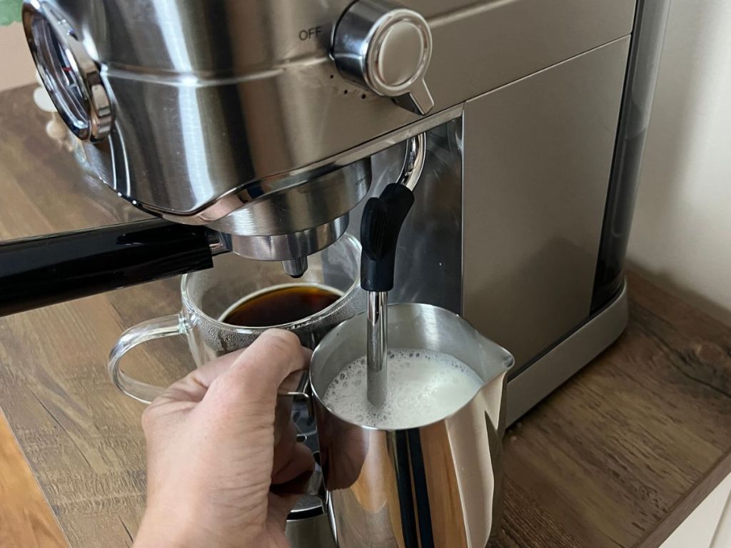 hand holding a frothing pitcher and using the steam wand attachment on side of the casabrews espresso maker
