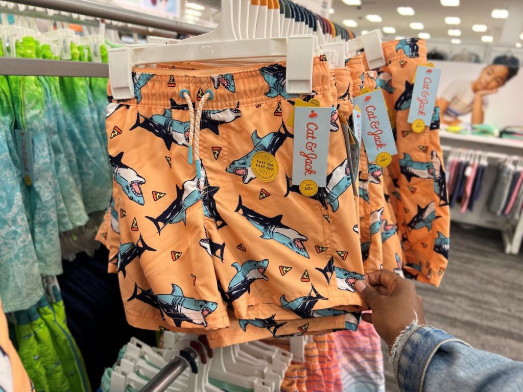 Hand holding a pair of orange swim shorts with sharks printed all over them
