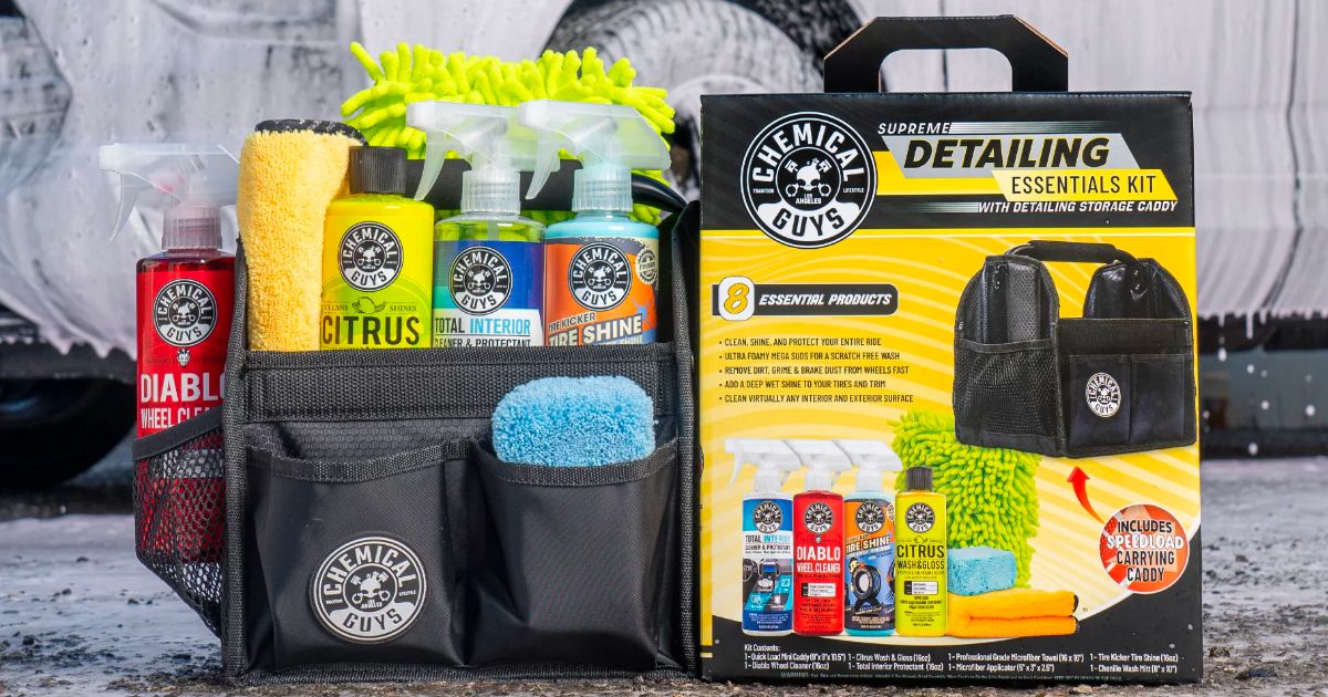 Chemical guys detailing kit sitting on a garage floor with a guy detailing a car in the background